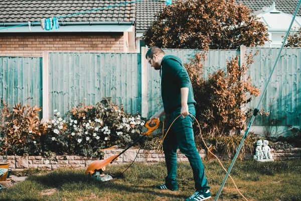Man Holding Orange Electric Grass Cutter on Lawn to conserve outdoor water